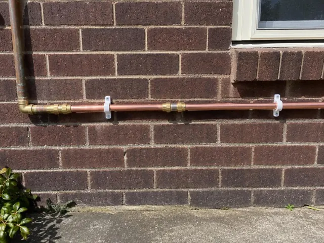 Copper water pipe repaired along a brick exterior wall beneath a window in Lindfield