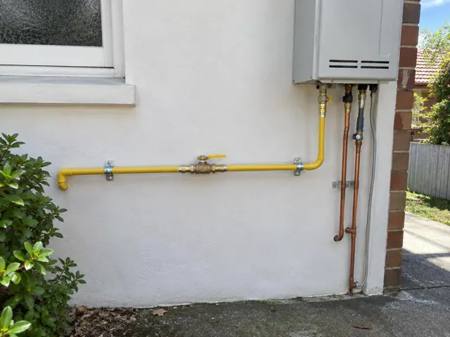 Yellow gas pipework and valve on an exterior house wall beside a hot water unit in Lindfield